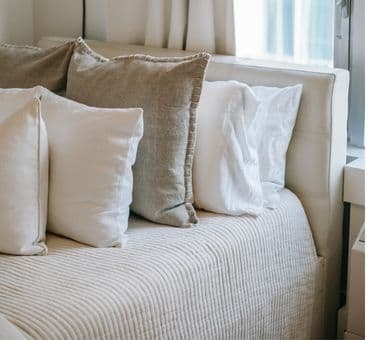 Minimal bir yatak odası ve yatağın üzerine dizilmiş çeyizlik yastıklar