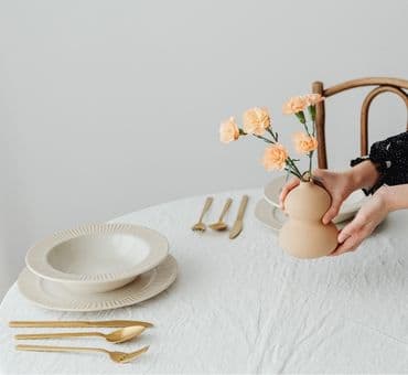 Porselen tabaklar, gold çatal bıçaklar ile zarif bir masaya seramik vazo içinde konulan çiçekler